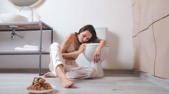 A woman throwing up in the bathroom with a cake put in front of her.